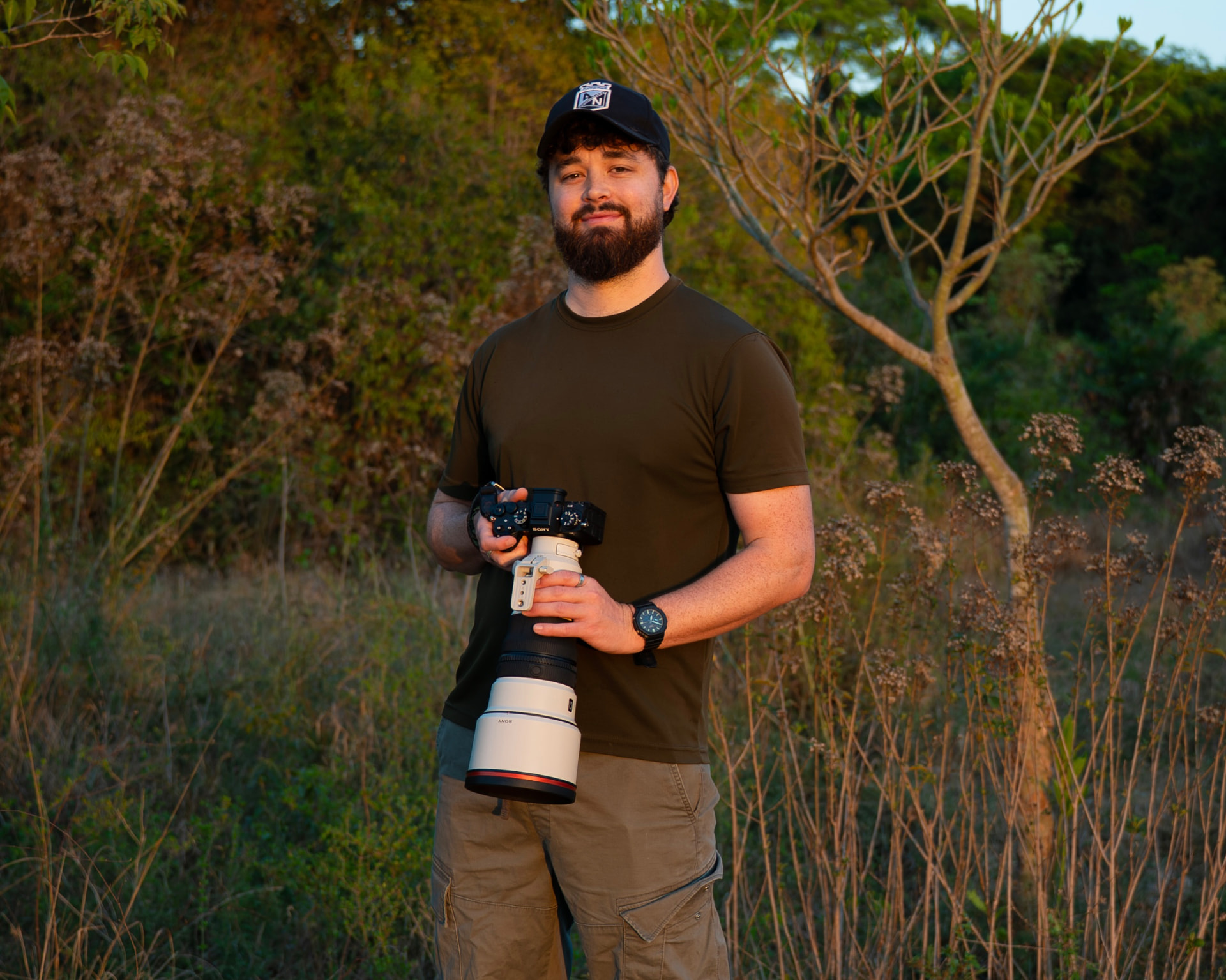 Charlie Page holding a camera with a large white telephoto lens in golden-hour scrubland